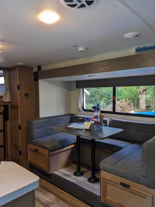 RV rental's inviting dinette: booth seating, table, and natural light create a cozy living space, ready for travel adventures.. Forest River Cherokee Grey Wolf 23DBH 2024