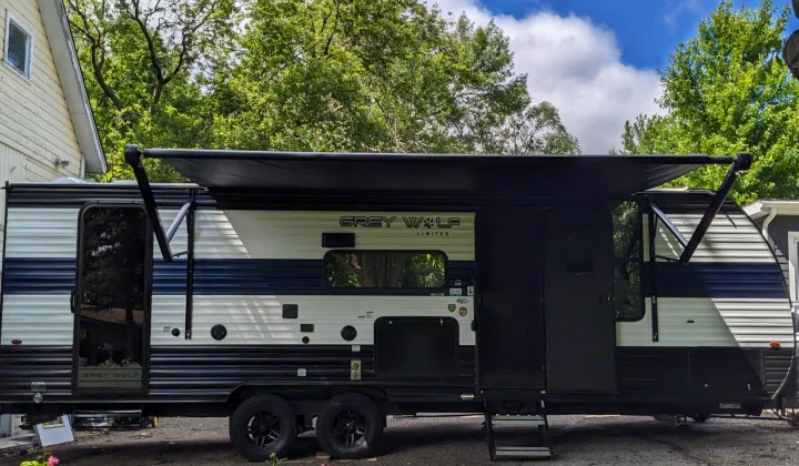 Side view of a modern black, white, and blue travel trailer with an extended awning, great for an rv rental.. Forest River Cherokee Grey Wolf 23DBH 2024