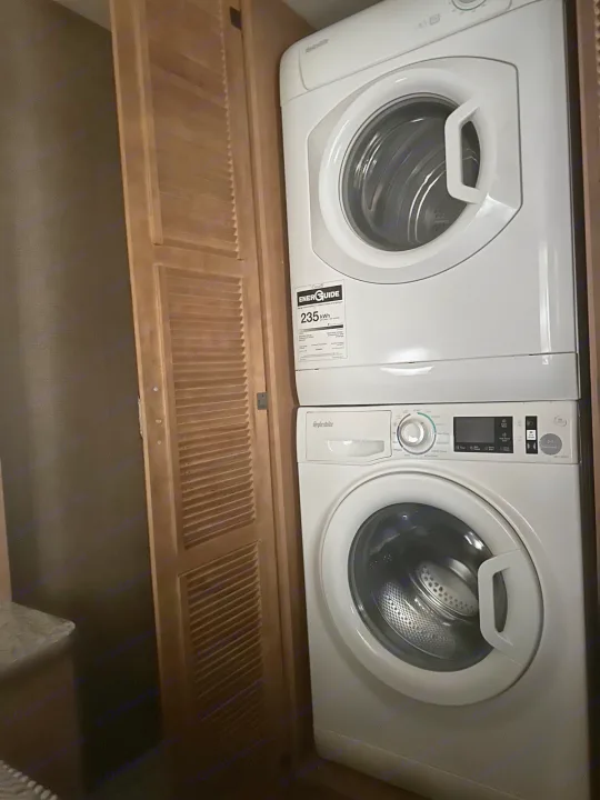 White stacked washer and dryer, common in an RV rental, installed next to wooden louvered doors.. Thor Hurricane 2017