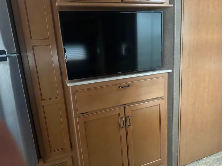 RV rental: RV interior displays a black flat-screen TV on light wood cabinetry, with a stainless steel fridge to the left.. Thor Hurricane 2017