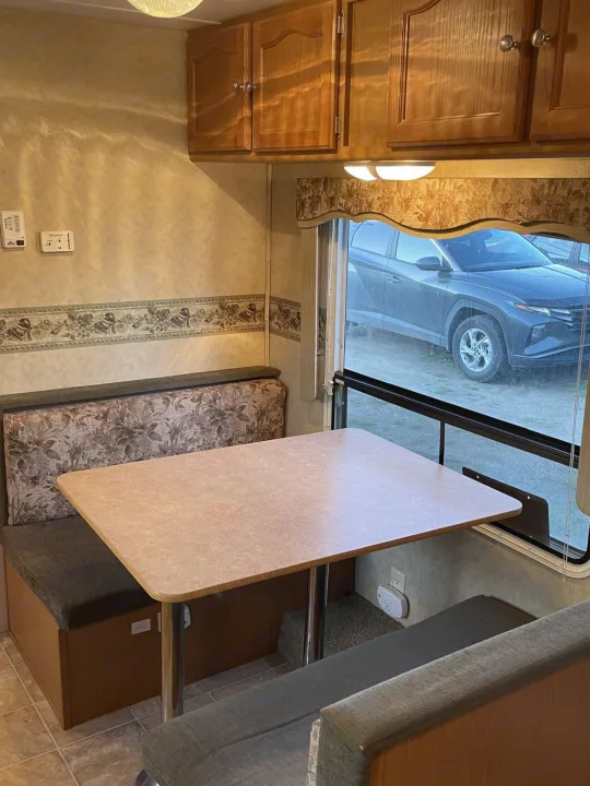 Inside an RV rental, a dinette area features bench seating, a table, wooden cabinets, and a window with an SUV parked outside.. Dutchmen Dutchmen 2007