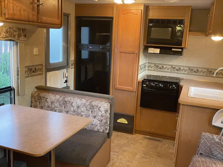 Spacious RV rental interior featuring a well-equipped kitchen with microwave, stove, and sink, plus a comfortable dining booth.. Dutchmen Dutchmen 2007