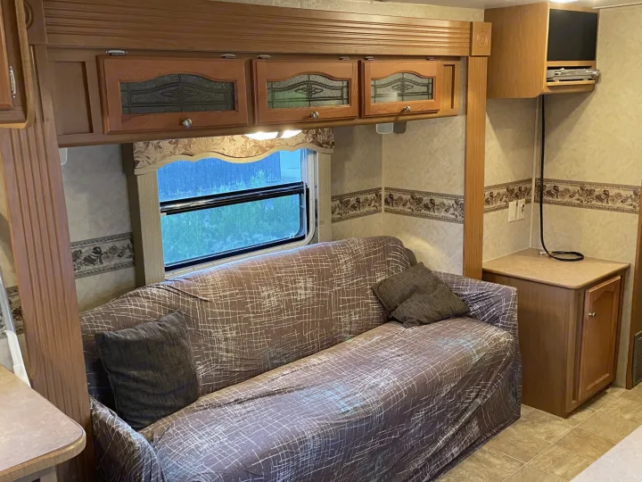 RV rental living room with a slipcovered couch, wood cabinets, TV, and patterned wallpaper.. Dutchmen Dutchmen 2007