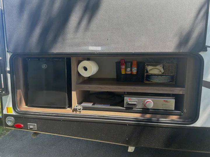 This RV rental's outdoor kitchen features a mini-fridge, paper towels, sprays, and a grill, ready for camping cooking!. Cruiser RV MPG 2500bh 2024