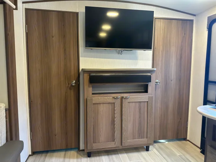 **RV rental** entertainment unit: TV, soundbar, storage cabinet, flanked by two wood-grain doors in a modern interior.. Cruiser RV MPG 2500bh 2024