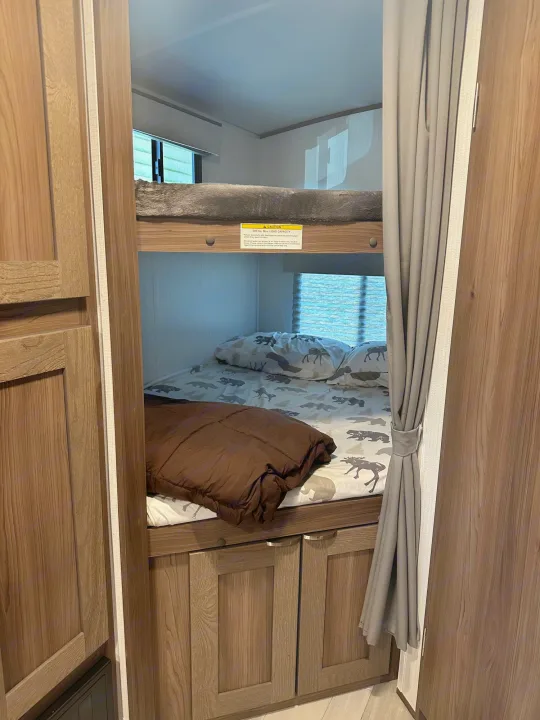 An RV rental's cozy bunk beds, with patterned bedding and a brown comforter, feature a visible 300 lbs. max load capacity sign.. Cruiser RV MPG 2500bh 2024