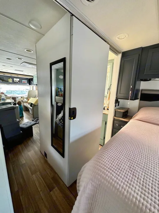 This RV rental interior shows a bedroom with a quilted bed, dark cabinets, and a mirrored sliding door to the living area and bathroom.. Thor Motor Coach A.C.E 2018