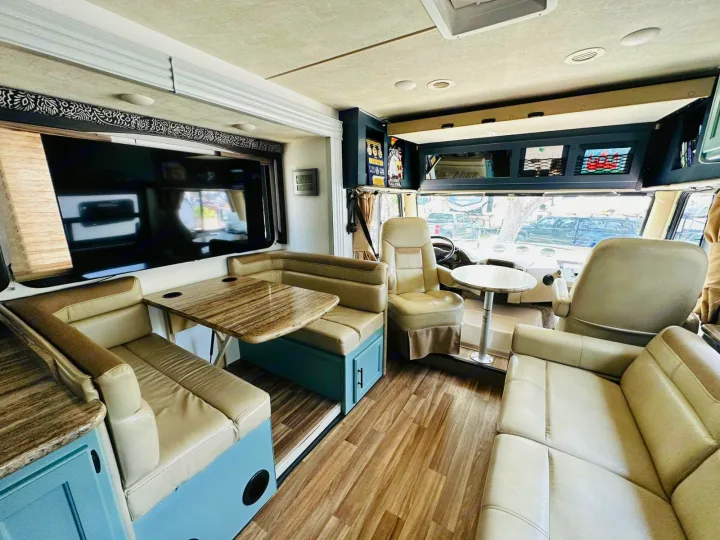 Inside a modern rv rental: spacious living area with U-shaped dinette, large TV, and comfortable swivel seats.. Thor Motor Coach A.C.E 2018