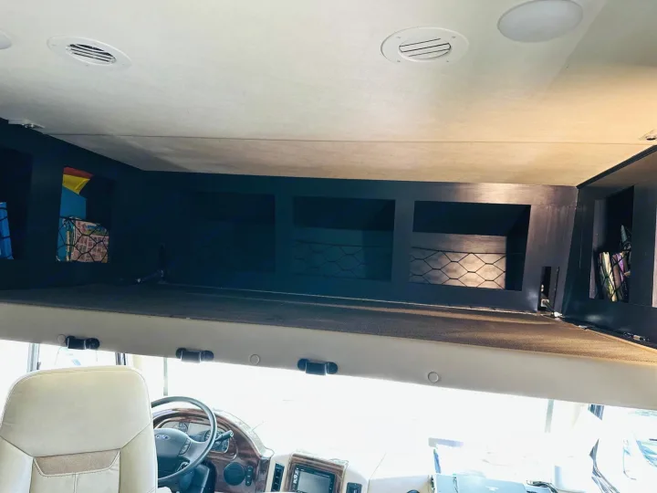 View inside an RV rental motorhome: an overhead bunk bed with dark storage cubbies above the front driver's area.. Thor Motor Coach A.C.E 2018