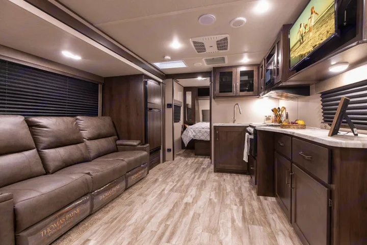 Explore this modern RV rental's spacious interior, featuring a comfy sofa, full kitchen, wall-mounted TV, and a bedroom.. Grand Design Transcend Xplor 221RB 2023