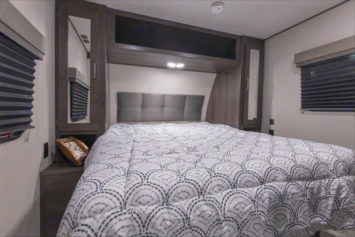 Cozy RV rental bedroom featuring a comfy bed, modern headboard, overhead cabinets, and compact storage.. Grand Design Transcend Xplor 221RB 2023