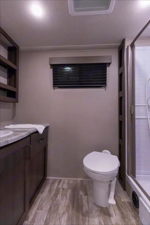 Inside an RV rental: a compact bathroom with a toilet, vanity, sink, and glass shower. Features light walls & wood-look floor.. Grand Design Transcend Xplor 221RB 2023