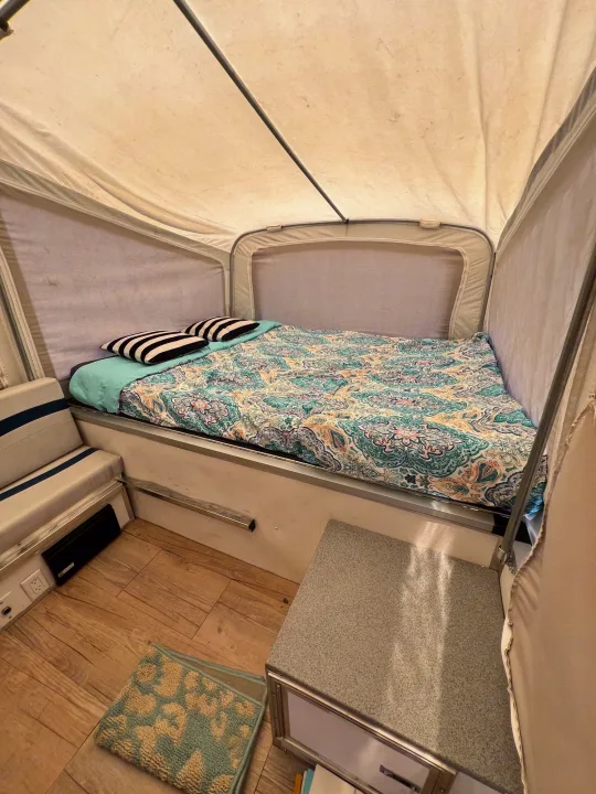 Inside an rv rental: a cozy pop-up camper bedroom with patterned bed, striped pillows, light wood floor, and seating.. Quicksilver Quicksilver Livin Lite 2011