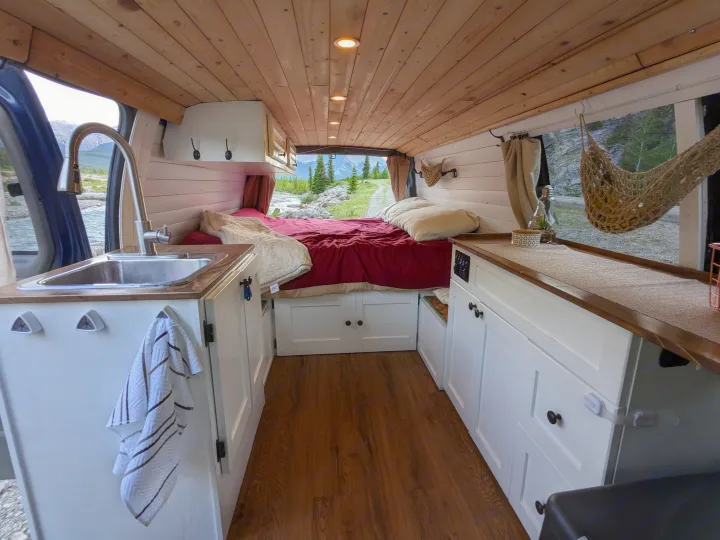 Cozy RV rental interior with a comfy bed, kitchen sink, and panoramic window views of mountains & a river.. Chevrolet Express 2003