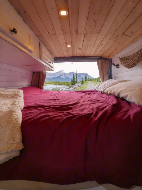 Cozy RV rental interior with a bed looking out to a mountain river view. Perfect for nature lovers.. Chevrolet Express 2003