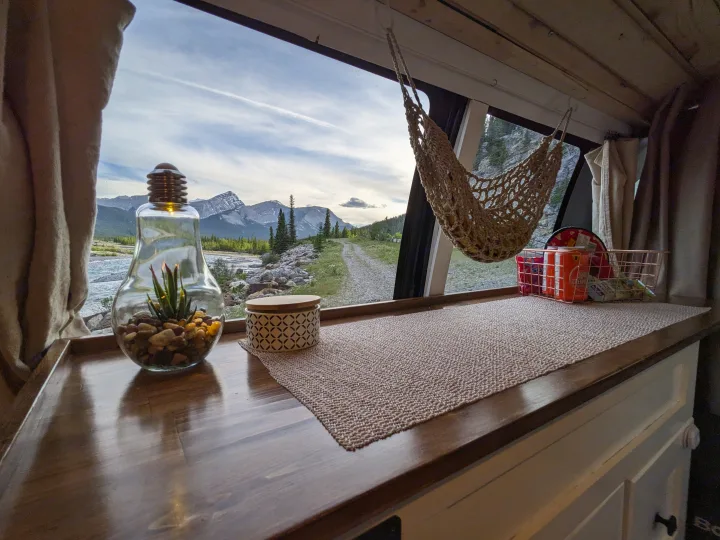 Scenic RV rental view: Mountains, river, & road from cozy interior with terrarium, snacks, and hanging net.. Chevrolet Express 2003