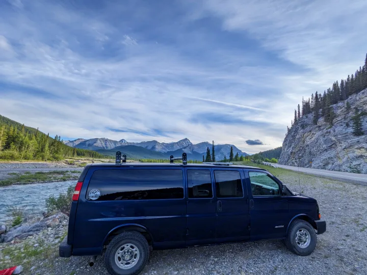 Dark blue RV rental van parked by a mountain river. Ideal for scenic road trips and outdoor adventures.. Chevrolet Express 2003