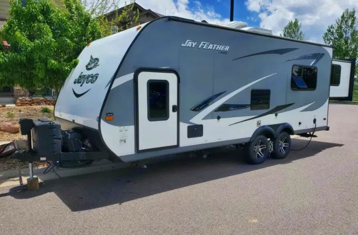 Grey and white Jayco Jay Feather travel trailer RV rental, parked on asphalt with a slide-out extended.. Jayco X213 2016