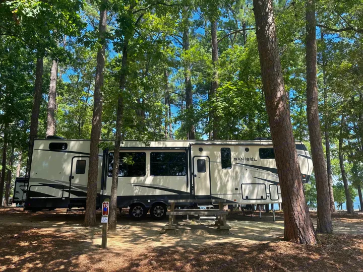 Modern RV rental at a scenic wooded campsite, featuring a picnic table and lake views.. Primetime Sanibel 3602WB 2023