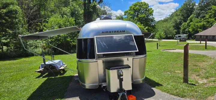Iconic silver Airstream travel trailer (a great RV rental option) parked at a sunny campsite with an extended awning & picnic table.. Airstream Caravel 2022