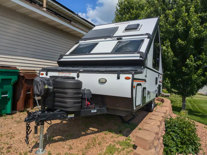 White A-frame RV rental with solar panels & black accents, parked on gravel next to a house. A compact travel trailer.. Rockwood A122s 2023