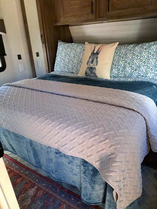 Serene RV rental bedroom featuring a comfy bed with a quilted comforter, blue patterned sheets, and a cute rabbit pillow.. Forest River Evo 2022