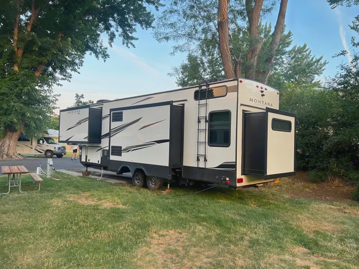 A large Montana RV is parked at a grassy campsite with slide-outs extended, ideal for an rv rental.. Keystone RV Montana High Country 2020