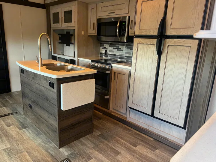 RV rental kitchen: modern island with sink, light-toned cabinetry, stove, microwave, and large refrigerator.. Keystone RV Montana High Country 2020