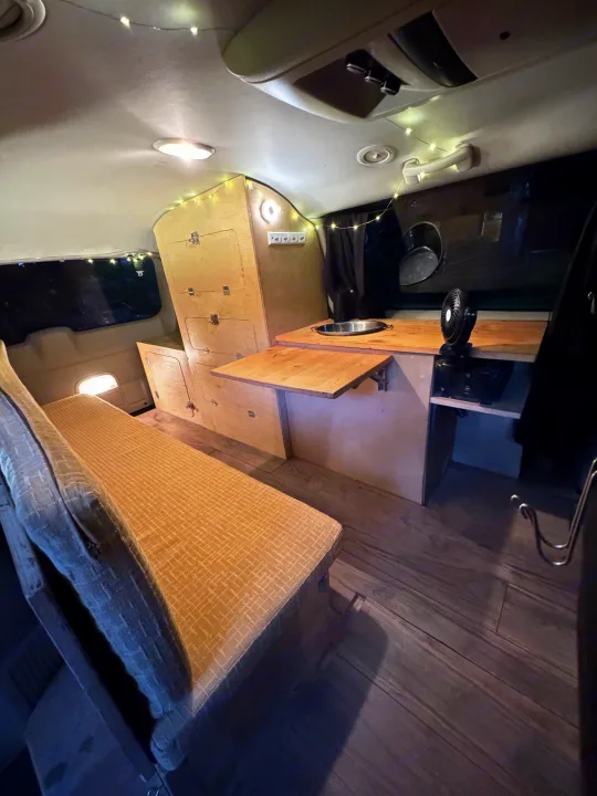 Cozy RV rental: a modern van conversion with custom wood interior, sink, bench bed, and ambient lights.. Dodge Grand Caravan 2013
