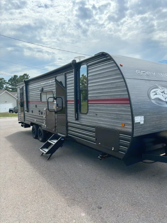 A spacious Grey Wolf travel trailer, ready for an RV rental adventure, parked on asphalt under a cloudy sky.. Forest River Cherokee 26DBH 2024