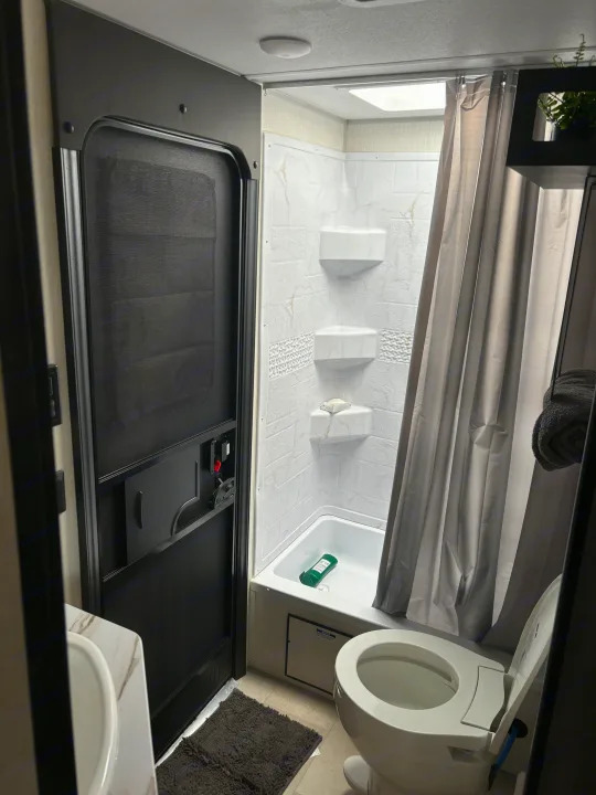 This RV rental bathroom offers a compact, functional space with a shower/tub, toilet, sink, and screen door.. Forest River Cherokee 26DBH 2024