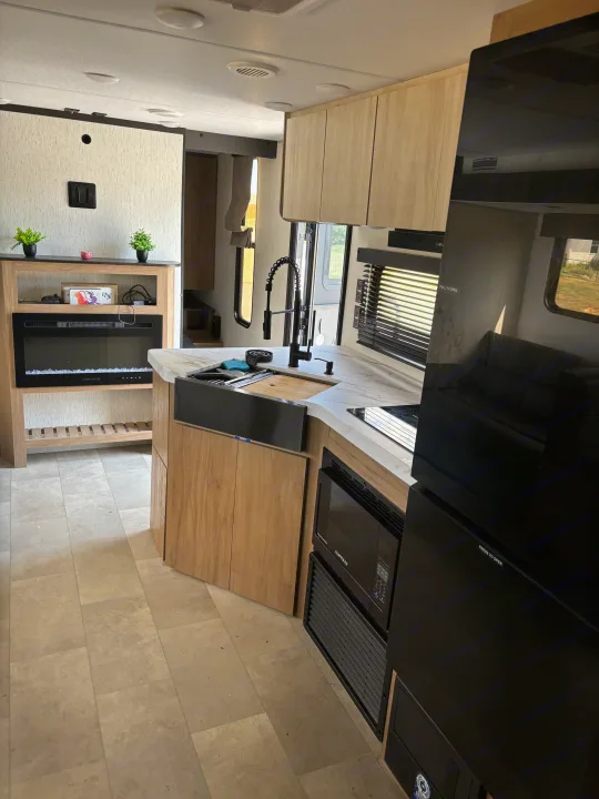 Modern RV rental interior with a fully equipped kitchen, including a sink, microwave, refrigerator, and cozy electric fireplace.. Forest River Cherokee 26DBH 2024