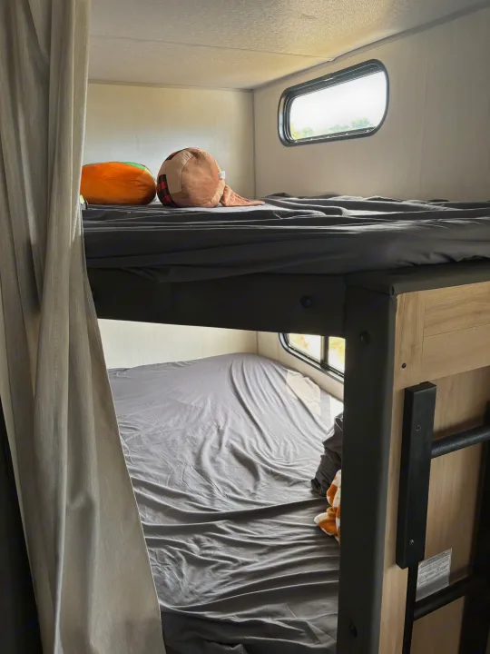 Inside an RV rental: comfortable bunk beds with gray bedding, pillows, and small windows, perfect for travel.. Forest River Cherokee 26DBH 2024