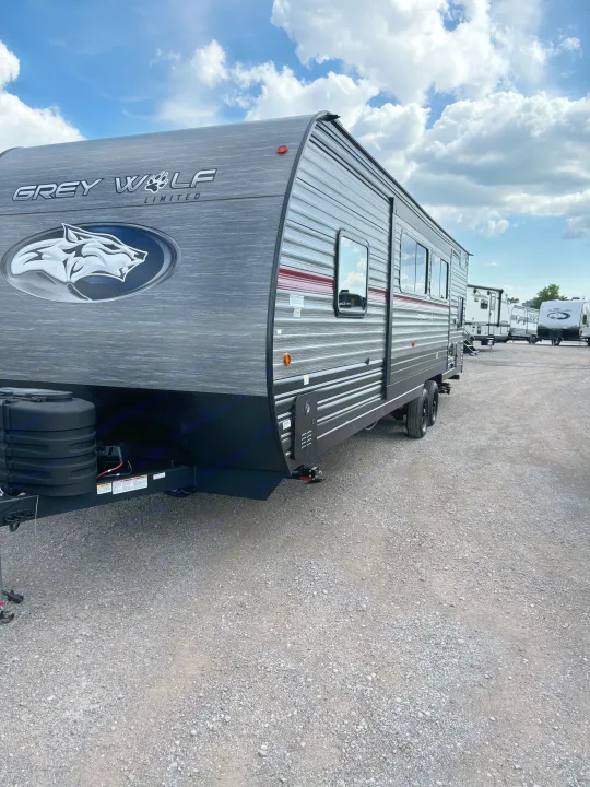A dark Grey Wolf travel trailer, ideal for an RV rental. Ready for camping adventures on a gravel lot with other RVs.. Forest River Cherokee 26DBH 2024