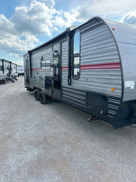 A sleek grey travel trailer for RV rental, parked on a gravel lot. Several similar campers are visible under a cloudy sky.. Forest River Cherokee 26DBH 2024