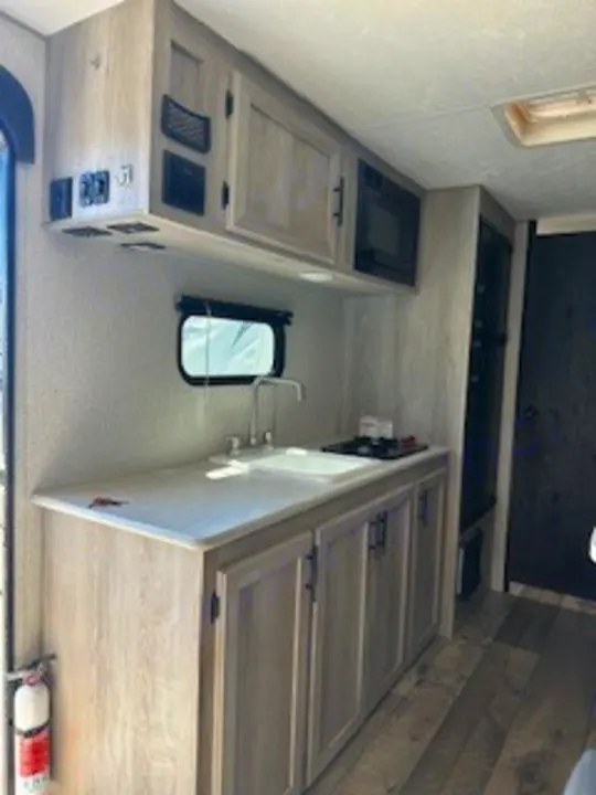 RV rental interior: A compact kitchenette with sink, stovetop, microwave, and wood-look cabinets for comfortable travel.. Sportsmen 181BH 2022