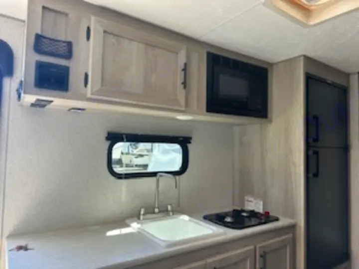 RV rental kitchen showing a sink, 2-burner stove, microwave, and fridge. Perfect for your travel adventures!. Sportsmen 181BH 2022