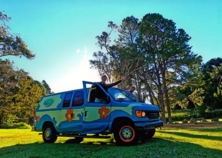 Brightly painted "Mystery Machine" style van for rv rental, parked on grass. Two men wave from inside, ready for adventure!. Ford E250 Eagle Camper 2006