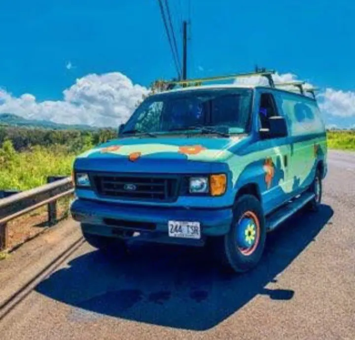 This vibrant, custom Mystery Machine-style Ford van, perfect for RV rental road trips, is parked on a scenic road under a blue sky.. Ford E250 Eagle Camper 2006
