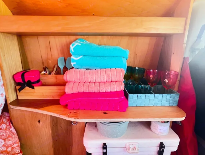 Thoughtful RV rental amenities: vibrant towels, utensils, & glassware neatly arranged in wooden shelving.. Ford E250 Eagle Camper 2006
