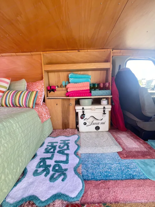 Vibrant RV rental interior: colorful bed, custom wood shelving with towels & cups, cooler, and playful rugs.. Ford E250 Eagle Camper 2006