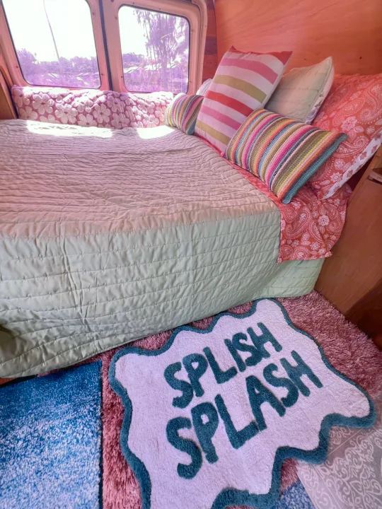 Relaxing RV rental interior featuring a bed with green comforter, colorful pillows, and a "Splish Splash" rug. Outside view.. Ford E250 Eagle Camper 2006