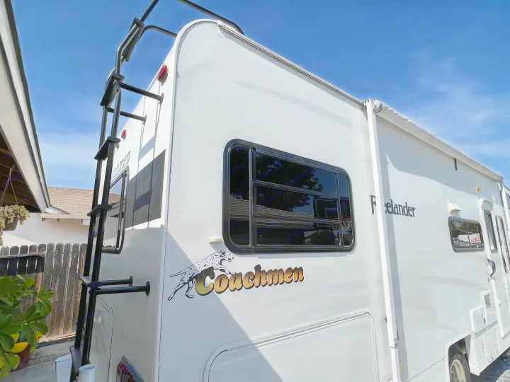White Coachmen Freelander RV for rv rental, showing its rear ladder, side window, and awning against a blue sky.. Coachmen Freelander 2007