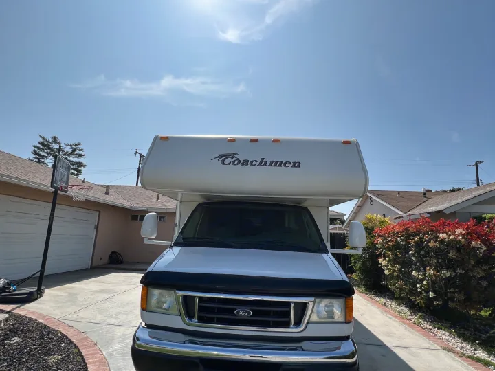 White Coachmen RV rental parked in a sunny driveway next to a basketball hoop. Ready for your next adventure!. Coachmen Freelander 2007