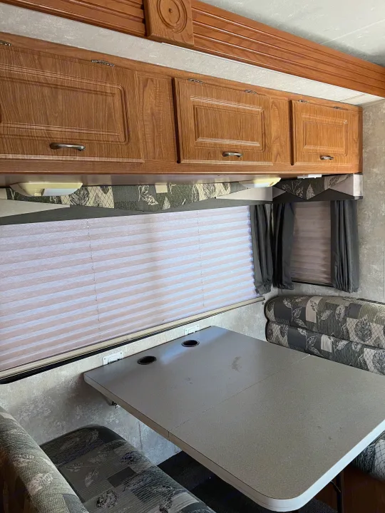 RV rental dinette: Cozy interior with wooden cabinets, window blinds, and patterned bench seating surrounding a table.. Coachmen Freelander 2007