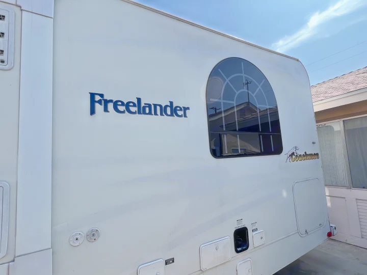 White Coachmen Freelander motorhome side, ready for RV rental. Features an arched window and lower utility hookups.. Coachmen Freelander 2007