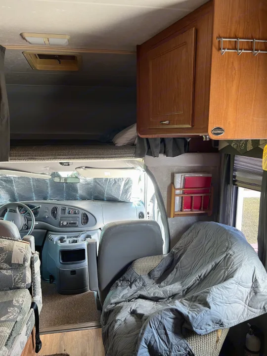 Interior of an RV rental: driver's cab, overhead bunk bed, and cabin seating with wood accents.. Coachmen Freelander 2007