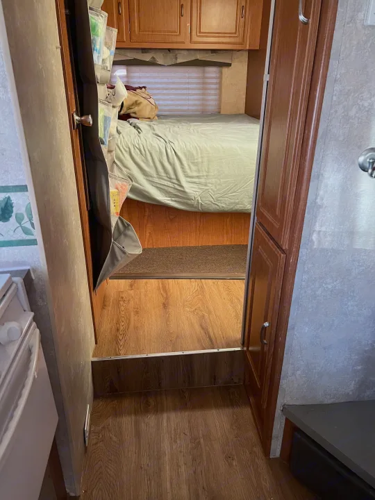 View from the living area into the cozy bedroom of an RV rental, featuring a bed and clever over-door storage.. Coachmen Freelander 2007
