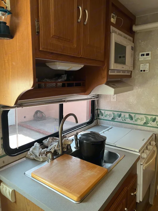 This RV rental kitchen features wood cabinets, a sink with faucet, microwave, & covered stove, perfect for meals on the go.. Coachmen Freelander 2007