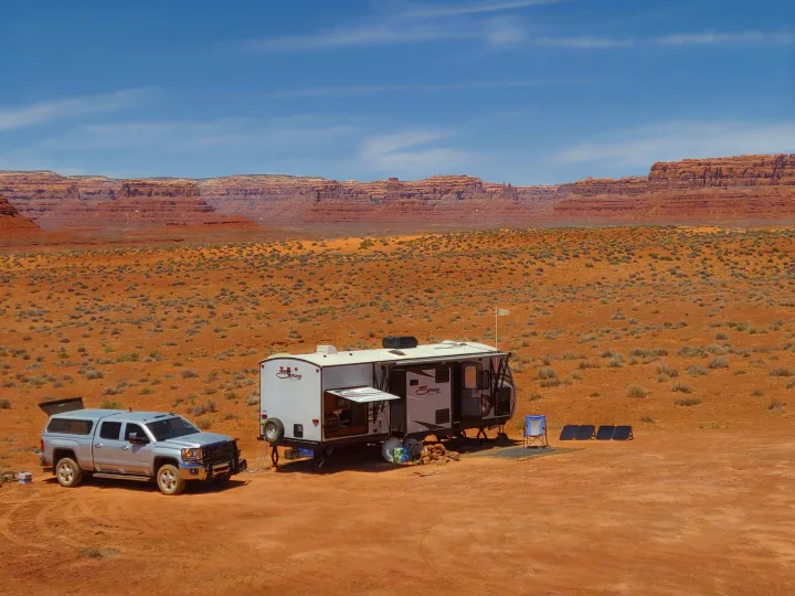 RV rental adventure: a pickup truck & travel trailer camped in a vast red desert with distant towering cliffs.. KZ Spree 301RIK 2015